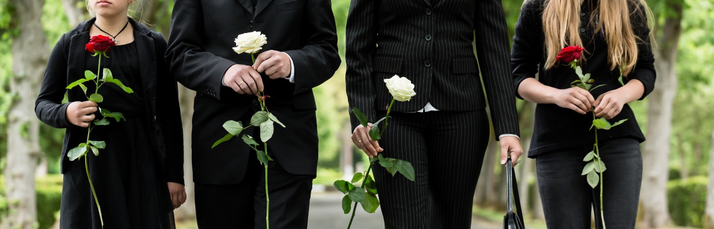 Four people at a funeral holding red roses and wearing black suits