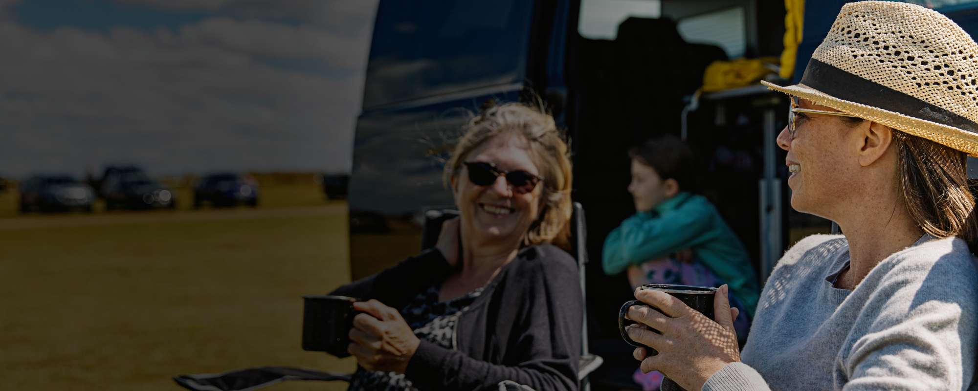Two ladies sitting outside camper van with mugs of tea